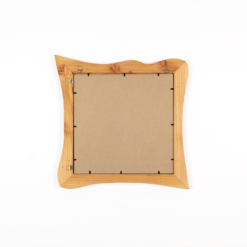 Peut inclure: Un cadre photo carr&eacute; en bois avec une finition naturelle en grain de bois brun clair et des bords ext&eacute;rieurs ondul&eacute;s et irr&eacute;guliers. Le dos du cadre pr&eacute;sente un panneau plat beige fix&eacute; par des clips m&eacute;talliques et deux attaches.