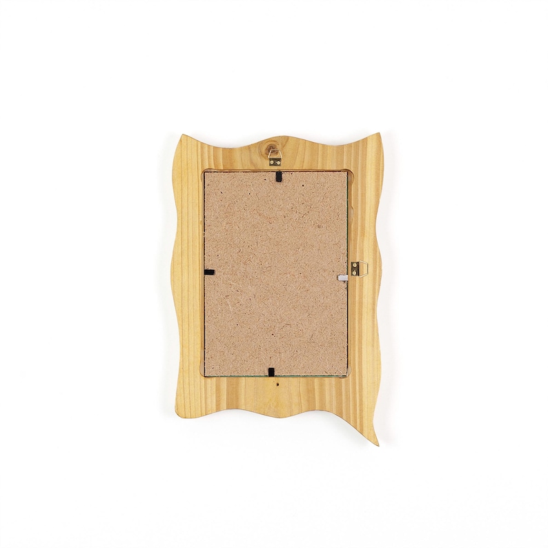 May include: A light-colored wooden picture frame with a wavy, decorative edge. The back of the frame is visible, showing a cardboard backing and metal hardware for hanging. The frame is designed to hold a rectangular photo.