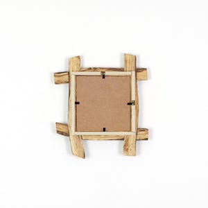 May include: A square picture frame constructed from light-colored wood with a natural grain pattern. The frame features a rustic, overlapping plank design and a flat, brown fiberboard backing secured with four small metal clips and a top hanger.