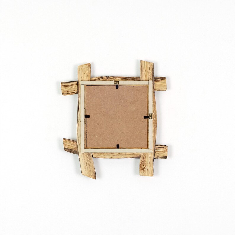 May include: A square picture frame constructed from light-colored wood with a natural grain pattern. The frame features a rustic, overlapping plank design and a flat, brown fiberboard backing secured with four small metal clips and a top hanger.