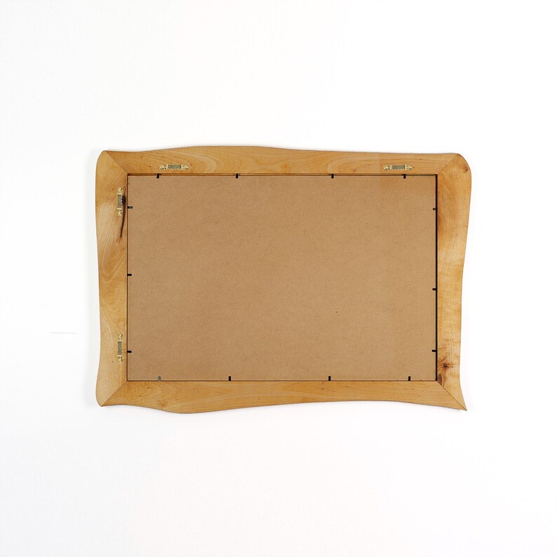 Peut inclure: Un cadre photo rectangulaire en bois avec une finition brun clair. Le cadre a une forme ondul&eacute;e et organique et un dos brun. Le mat&eacute;riel de suspension en m&eacute;tal est fix&eacute; &agrave; l'arri&egrave;re.