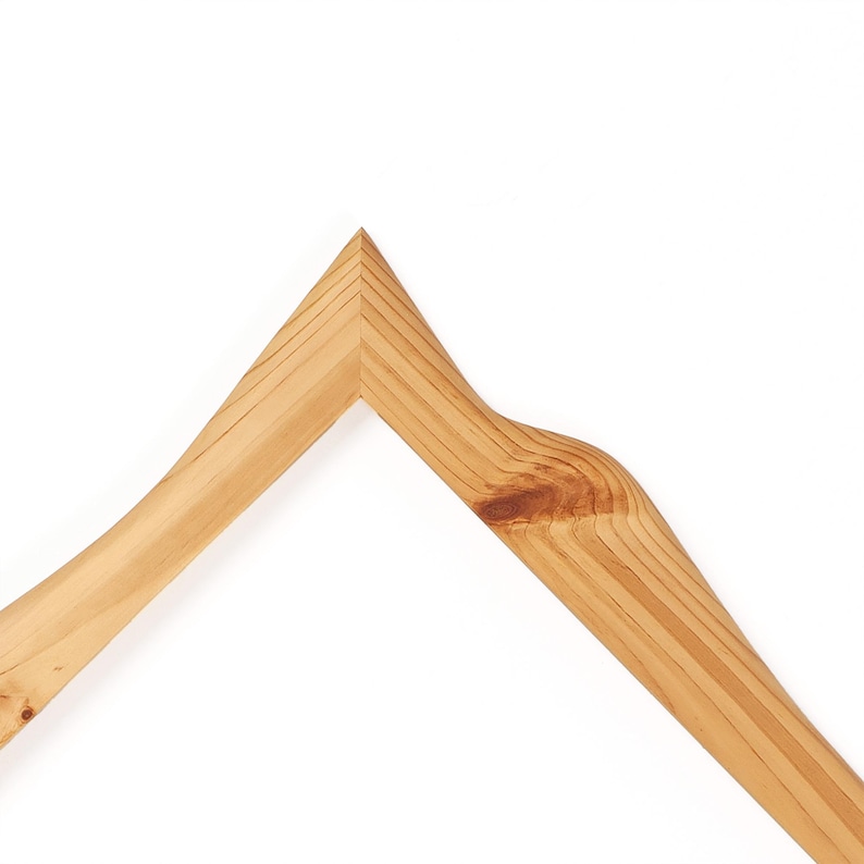 K&ouml;nnte beinhalten: Ein hellbrauner Holzkleiderb&uuml;gel mit einem markanten V-f&ouml;rmigen Oberteil, sichtbarer nat&uuml;rlicher Holzmaserung und einem auff&auml;lligen dunklen Astloch am rechten Arm, der eine glatte Oberfl&auml;che und eine stabile, abgewinkelte Konstruktion aufweist.