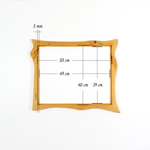 May include: A rectangular wooden frame with an irregular, wavy outer edge. The frame features metal mounting hardware on the back. Dimensions indicated are 5 mm thickness, with internal measurements of 49 cm by 39 cm and external measurements of 50 cm by 40 cm.
