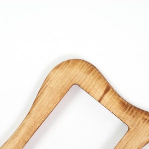 May include: A close-up shot of a wooden clothes hanger. The light-coloured wood has visible grain and a curved design. The hanger features a rectangular cutout near the top.