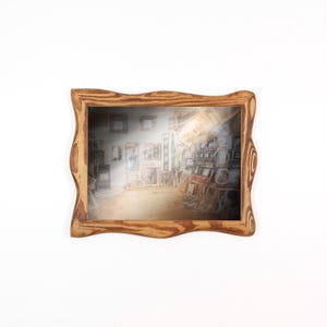 May include: A wooden framed mirror with a wavy edge. The mirror reflects a room filled with artwork and shelves. The frame is light brown, and the reflection has a warm glow. The mirror is rectangular in shape.