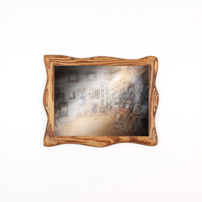 May include: A wooden framed mirror with a wavy edge. The mirror reflects a room filled with artwork and shelves. The frame is light brown, and the reflection has a warm glow. The mirror is rectangular in shape.