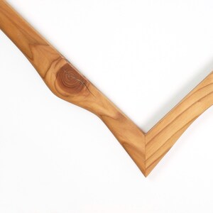 May include: A V-shaped wooden frame corner piece made of light brown wood with a visible natural grain pattern and a prominent circular knot detail on the left side. The wood features smooth, finished surfaces and a sharp, angled mitered joint.