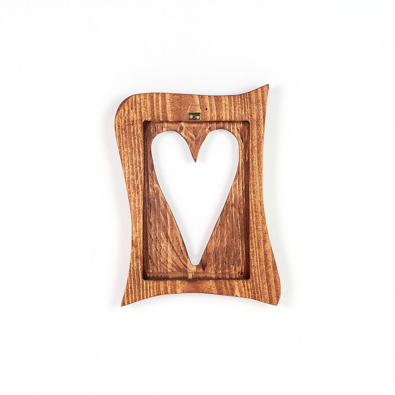 May include: A wooden picture frame with a heart-shaped cutout. The frame is a warm brown color and has a wavy, decorative edge. A small metal hanger is attached to the top for wall mounting.