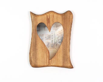 May include: A rectangular wooden picture frame with a natural light brown wood grain finish and a wavy, irregular outer edge. The frame features a central heart-shaped cutout opening, showcasing a visible wood texture throughout the surface.
