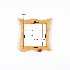 Puede incluir: Un marco de fotos de madera de color marr&oacute;n claro con un borde exterior ondulado y una abertura interior cuadrada. El marco presenta una veta de madera visible y un soporte met&aacute;lico en el borde superior. Las medidas son 5 mm, 14 cm y 15 cm.