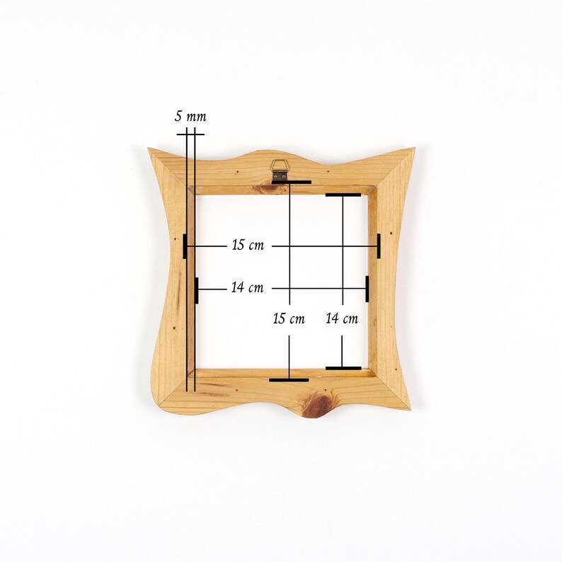 Puede incluir: Un marco de fotos de madera de color marr&oacute;n claro con un borde exterior ondulado y una abertura interior cuadrada. El marco presenta una veta de madera visible y un soporte met&aacute;lico en el borde superior. Las medidas son 5 mm, 14 cm y 15 cm.