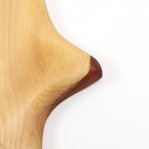 Peut inclure: Gros plan sur une planche &agrave; d&eacute;couper en bois avec un motif de grain naturel. La planche est de couleur brun clair avec un bord brun fonc&eacute;. La planche est fa&ccedil;onn&eacute;e avec un bord incurv&eacute;.