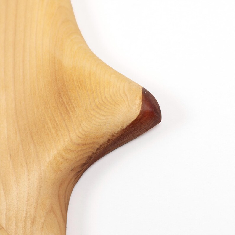 Peut inclure: Gros plan sur une planche &agrave; d&eacute;couper en bois avec un motif de grain naturel. La planche est de couleur brun clair avec un bord brun fonc&eacute;. La planche est fa&ccedil;onn&eacute;e avec un bord incurv&eacute;.