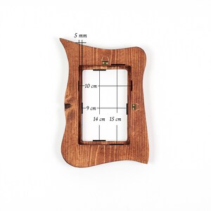 Peut inclure: Un cadre photo en bois brun avec un bord ext&eacute;rieur irr&eacute;gulier et ondul&eacute;. Le cadre pr&eacute;sente un grain de bois visible et des fixations m&eacute;talliques. Des annotations techniques indiquent une &eacute;paisseur de 5 mm et des dimensions int&eacute;rieures de 10 cm par 14 cm et 9 cm par 15 cm.