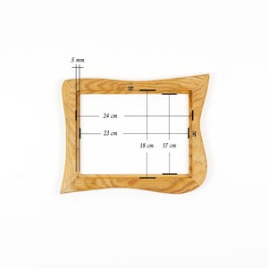 May include: A light brown wooden picture frame with a wavy, organic outer edge. The frame features technical measurement lines and text indicating a 5 mm thickness, with internal dimensions of 24 cm by 23 cm and 18 cm by 17 cm clearly marked.