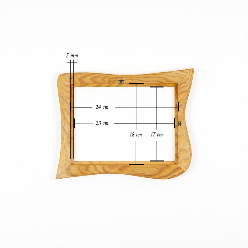 May include: A light brown wooden picture frame with a wavy, organic outer edge. The frame features technical measurement lines and text indicating a 5 mm thickness, with internal dimensions of 24 cm by 23 cm and 18 cm by 17 cm clearly marked.