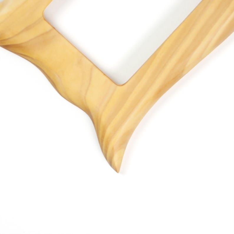 May include: A light tan wooden picture frame with a smooth, polished surface and a distinct, flowing grain pattern. The frame features a rectangular opening and a curved, organic edge design that tapers to a point at the bottom corner.