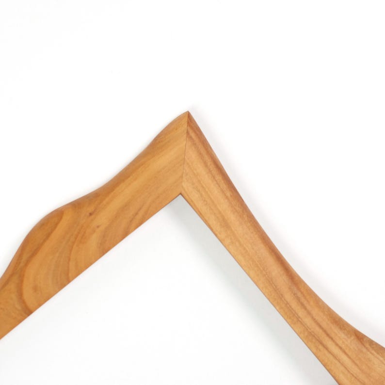 Op de afbeelding: Een houten kledinghanger met een gebogen ontwerp. De hanger is gemaakt van lichtbruin hout en heeft een gladde afwerking. De haak is niet zichtbaar. De achtergrond is wit.