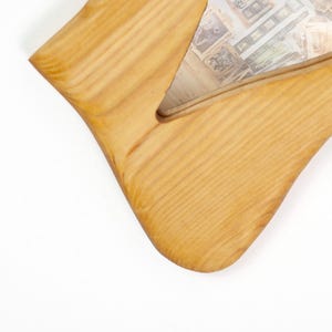Puede incluir: Un marco de fotos de madera de color claro con un dise&ntilde;o curvo &uacute;nico. El marco tiene una veta de madera natural y un recorte en el centro, que revela un vistazo de la imagen en el interior. Los bordes del marco son lisos y redondeados.