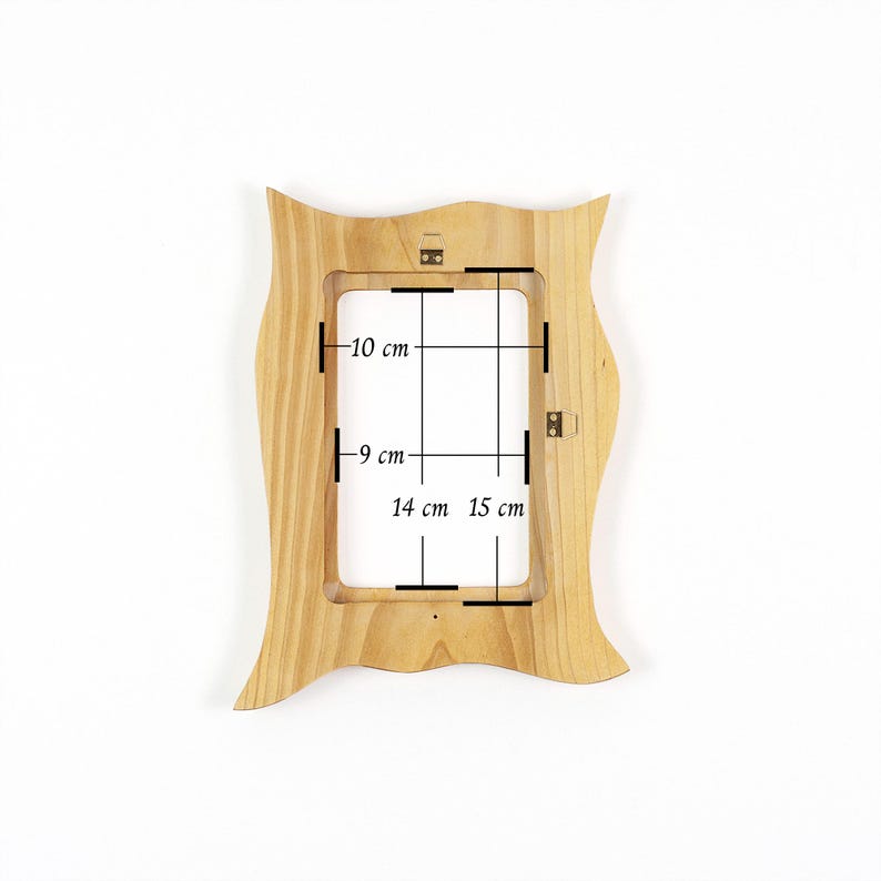 May include: A light-colored wooden picture frame with a wavy, organic outer edge. The frame features internal dimensions marked with black lines and text indicating measurements of 10 cm, 9 cm, 14 cm, and 15 cm. Metal hanging hardware is attached.