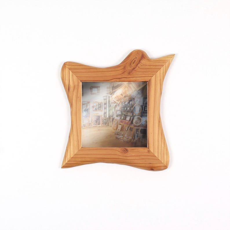 Pu&ograve; includere: Una cornice quadrata realizzata in legno marrone chiaro con un bordo esterno naturale, irregolare e ondulato. La cornice presenta una venatura del legno pronunciata e contiene una fotografia che ritrae una stanza piena di opere d'arte incorniciate.