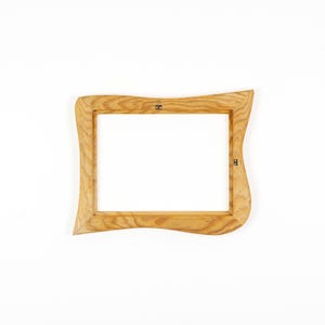 May include: A rectangular picture frame crafted from light-colored wood with a prominent grain pattern. The frame features an irregular, wavy outer edge design and includes small metal hardware attachments on the inner side for mounting purposes.