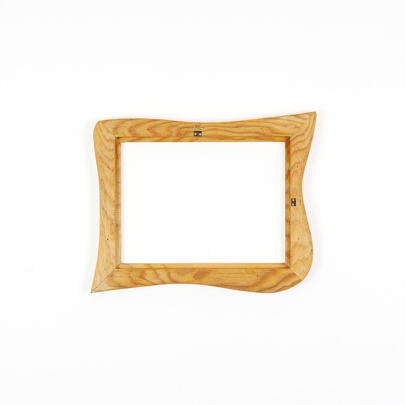 May include: A rectangular picture frame crafted from light-colored wood with a prominent grain pattern. The frame features an irregular, wavy outer edge design and includes small metal hardware attachments on the inner side for mounting purposes.