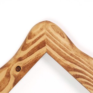 K&ouml;nnte beinhalten: Nahaufnahme eines Kleiderb&uuml;gels aus Holz. Der Kleiderb&uuml;gel besteht aus hellbraunem Holz mit einer dunkleren Beize, die die Holzmaserung hervorhebt. Die Eckverbindung ist sichtbar, und ein kleiner Knoten ist vorhanden.