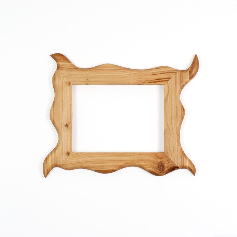 Puede incluir: Un marco de fotos rectangular hecho de madera de color marr&oacute;n claro con un patr&oacute;n de veta natural. El marco presenta un borde exterior irregular y ondulado con esquinas puntiagudas que se extienden hacia afuera, rodeando una abertura central.