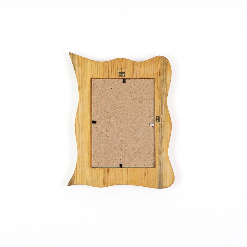 May include: Wooden picture frame with a wavy, irregular edge. The frame is made of light-colored wood with a natural grain pattern. The back of the frame is visible, showing a cardboard backing and hanging hardware.