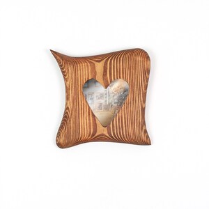 Puede incluir: Un marco de fotos cuadrado de madera con un patr&oacute;n de veta de madera marr&oacute;n oscuro y un recorte en forma de coraz&oacute;n en el centro. El marco presenta lados curvos y c&oacute;ncavos con esquinas redondeadas, creando una forma de coj&iacute;n distintiva.