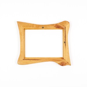 Peut inclure: Un cadre photo rectangulaire en bois avec une finition naturelle. Le cadre pr&eacute;sente un design ondul&eacute; unique sur les c&ocirc;t&eacute;s et est en bois brun clair. Le cadre est vide, avec un fond blanc visible &agrave; travers l'ouverture.