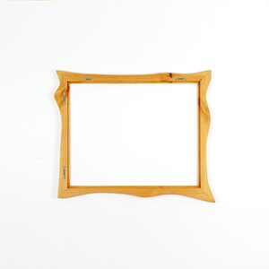 May include: A rectangular wooden picture frame with a light brown natural wood grain finish. The frame features wavy, organic edges on the left and right sides. Metal hanging hardware is attached to the back of the frame on the top and side.