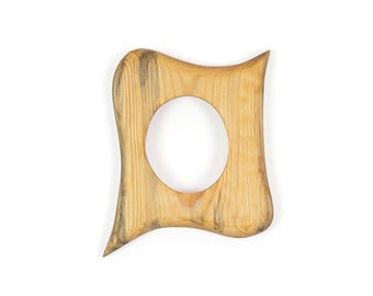 May include: A light brown wooden object with a smooth, curved, irregular shape and a central circular cutout. The wood features visible grain patterns and darker, greyish streaks throughout the surface, creating a natural, textured appearance.