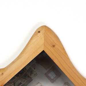 May include: A wooden picture frame with a unique, curved design. The frame is made of light-colored wood and has a clear glass or plastic cover. The frame's shape is reminiscent of a mountain peak. The frame is empty.