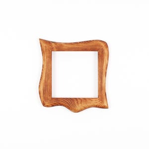 May include: A square wooden picture frame with a distinctive, undulating edge. The frame is crafted from light brown wood, showcasing a natural wood grain. The frame is empty, revealing a white background through the aperture.