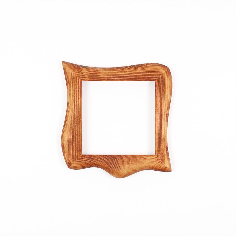 May include: A square wooden picture frame with a distinctive, undulating edge. The frame is crafted from light brown wood, showcasing a natural wood grain. The frame is empty, revealing a white background through the aperture.