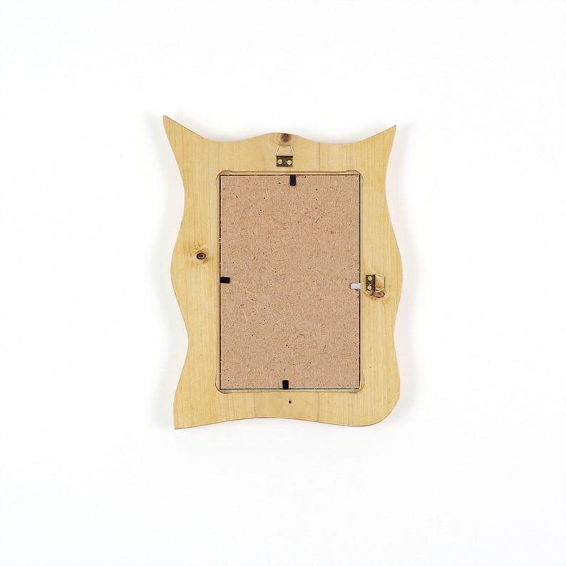 Pu&ograve; includere: Il retro di una cornice portafoto in legno chiaro con un bordo ondulato e sagomato. La cornice presenta un pannello posteriore rettangolare in fibra di legno compressa, fissato da piccole clip metalliche, e include un gancio metallico in alto al centro.