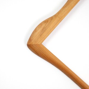 May include: A light brown wooden clothes hanger featuring a smooth, polished finish with visible natural wood grain patterns. The hanger has a curved shoulder design and a sturdy, angled frame construction, showcasing a warm, honey-toned wood texture.