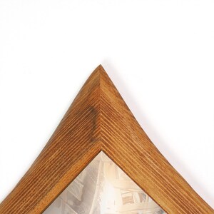 Peut inclure: Un cadre photo en bois de forme triangulaire. Le cadre est en bois brun clair avec un motif de grain visible. Le coin du cadre est pointu. L'int&eacute;rieur contient une image floue.