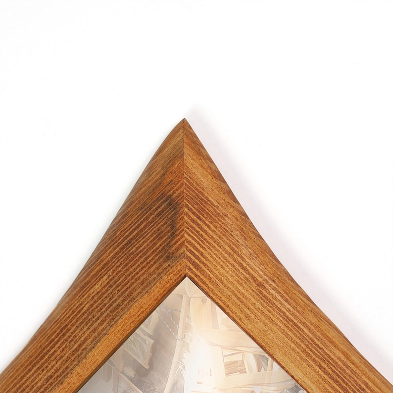 Peut inclure: Un cadre photo en bois de forme triangulaire. Le cadre est en bois brun clair avec un motif de grain visible. Le coin du cadre est pointu. L'int&eacute;rieur contient une image floue.