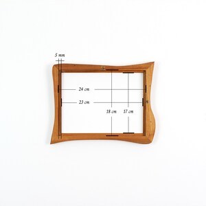 May include: A rectangular wooden picture frame with wavy, organic edges. The frame features internal dimensions of 24 cm by 18 cm and 23 cm by 17 cm, with a 5 mm thickness. A small metal hanging bracket is attached to the top centre of the frame.