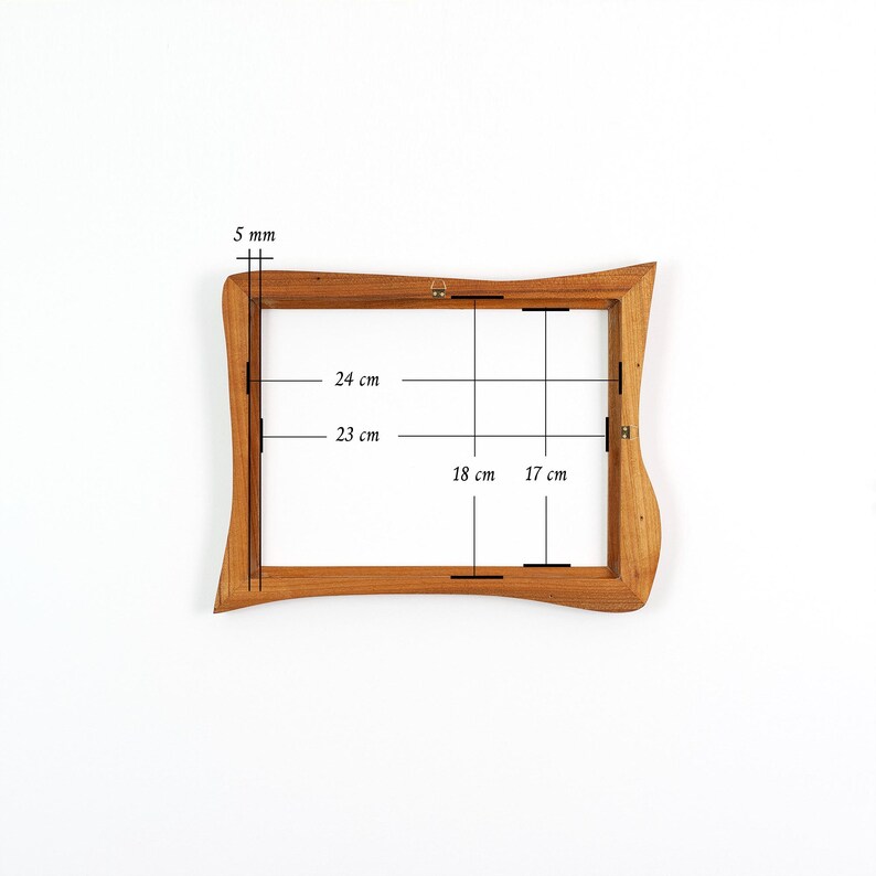 May include: A rectangular wooden picture frame with wavy, organic edges. The frame features internal dimensions of 24 cm by 18 cm and 23 cm by 17 cm, with a 5 mm thickness. A small metal hanging bracket is attached to the top centre of the frame.