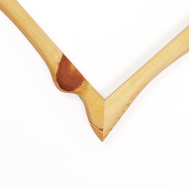 May include: A V-shaped wooden frame corner featuring light tan wood grain with a prominent, dark reddish-brown circular knot detail on the left side. The two pieces of wood are joined at a sharp angle, showcasing natural wood textures and patterns.