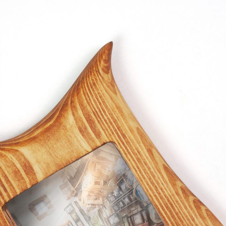 Puede incluir: Un marco de fotos de madera con un acabado marr&oacute;n claro y un patr&oacute;n de veta de madera natural prominente. El marco presenta un dise&ntilde;o de esquina puntiaguda y contiene una fotograf&iacute;a que muestra una colecci&oacute;n de varios cuadros en una pared.