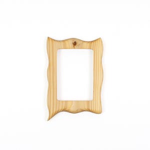 May include: A light-colored wooden picture frame with a wavy, ornate design. The frame has a rectangular opening and a natural wood grain finish. The frame is set against a white background.