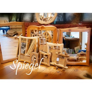 May include: A collection of wooden framed mirrors in various shapes and sizes, displayed on a wooden floor. The mirrors have natural wood finishes and are arranged in a shop setting. The word "Spiegel" is written in white script.