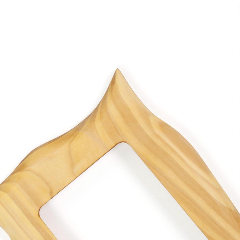 May include: A light brown wooden frame with a smooth, polished finish and a distinct grain pattern. The frame features a sharp, pointed corner at the top and curved, flowing edges that create an open, angular shape with a hollow center.