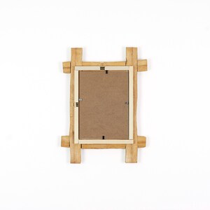 Pode incluir: Uma moldura retangular vista de tr&aacute;s, com uma borda de madeira natural castanho-claro e cantos salientes. O centro consiste num painel de fibra castanho plano, fixado com pequenos clipes met&aacute;licos e um gancho para pendurar na parede.