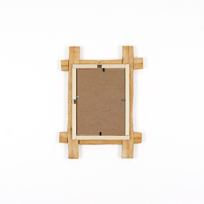 Pode incluir: Uma moldura retangular vista de tr&aacute;s, com uma borda de madeira natural castanho-claro e cantos salientes. O centro consiste num painel de fibra castanho plano, fixado com pequenos clipes met&aacute;licos e um gancho para pendurar na parede.